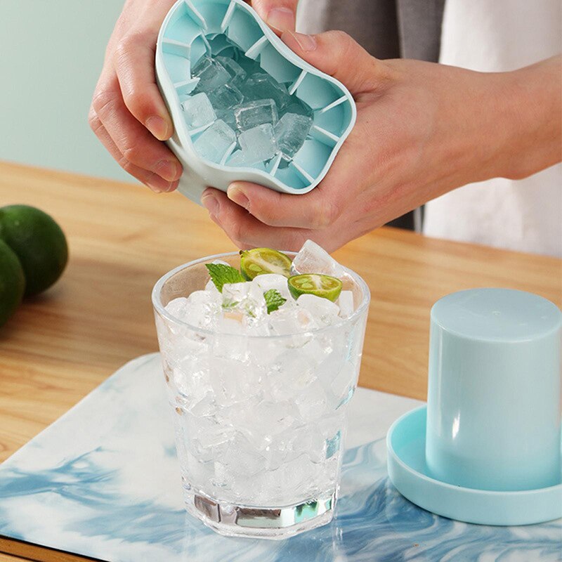 Person pouring ice cubes from a blue ice cube tray into a glass with lime and mint.